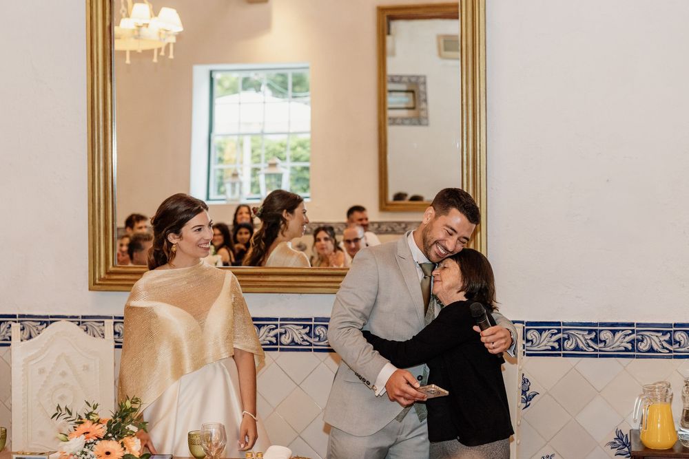 Bride and groom share a joyful moment with a guest at their wedding reception in an elegant venue with blue tile walls.