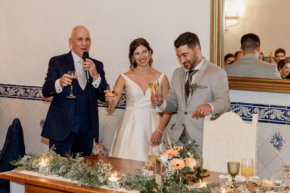 Bride and groom toast with elderly guest at elegant wedding reception with floral table decor.