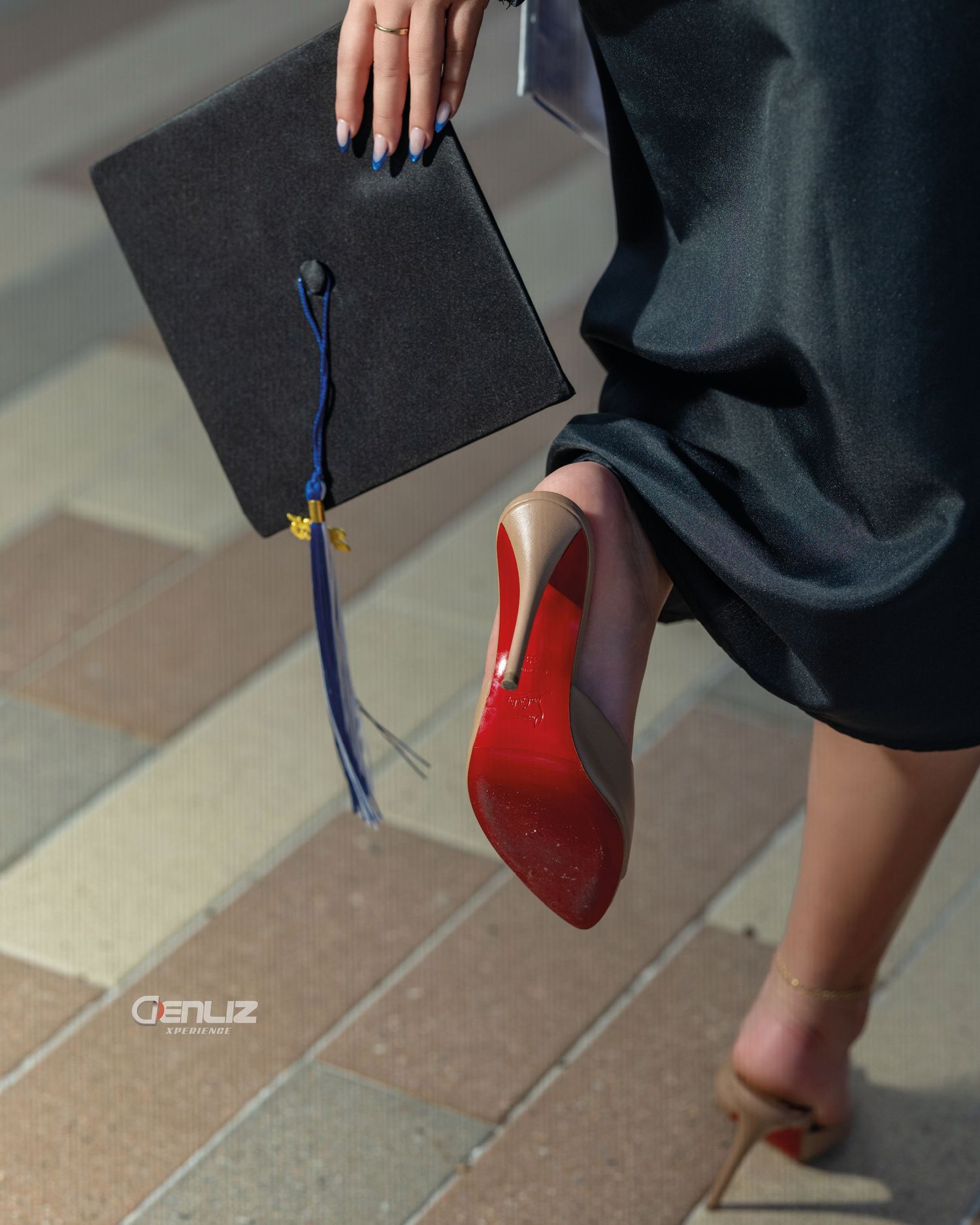 Graduate holding mortarboard cap with blue tassel, wearing red Christian Louboutin heels and academic gown.