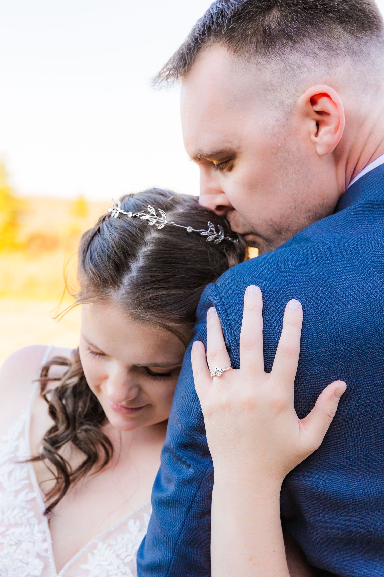 Close-up of tender wedding moment with bride showing ring while embracing groom.