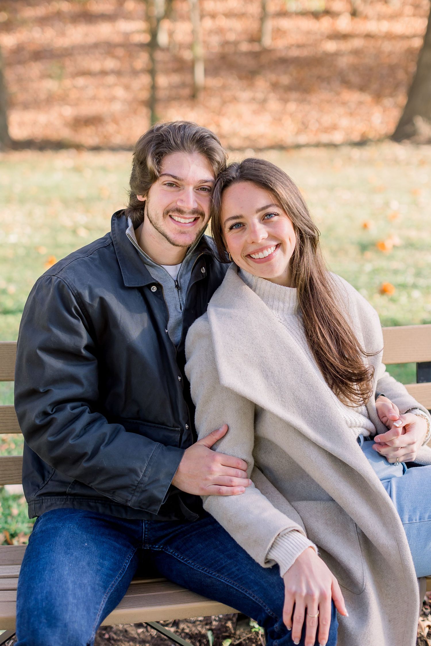 Couple sitting on a park bench surrounded by fallen autumn leaves.