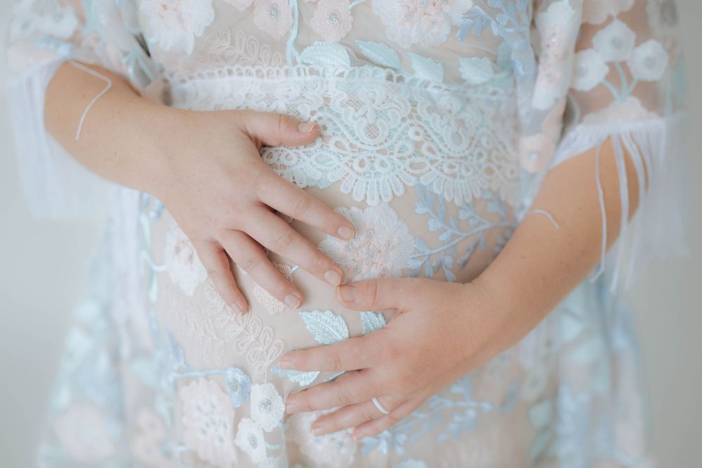 Close-up of hands gently resting on a lace-covered baby bump in a delicate floral maternity dress.