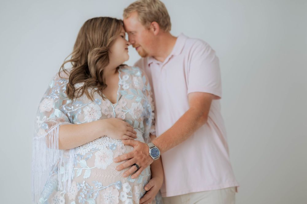 An intimate moment between expectant parents wearing soft pastels during a maternity photoshoot.
