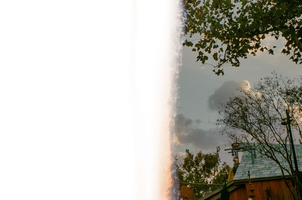 Trees and buildings photographed against cloudy sky with light leak effect.