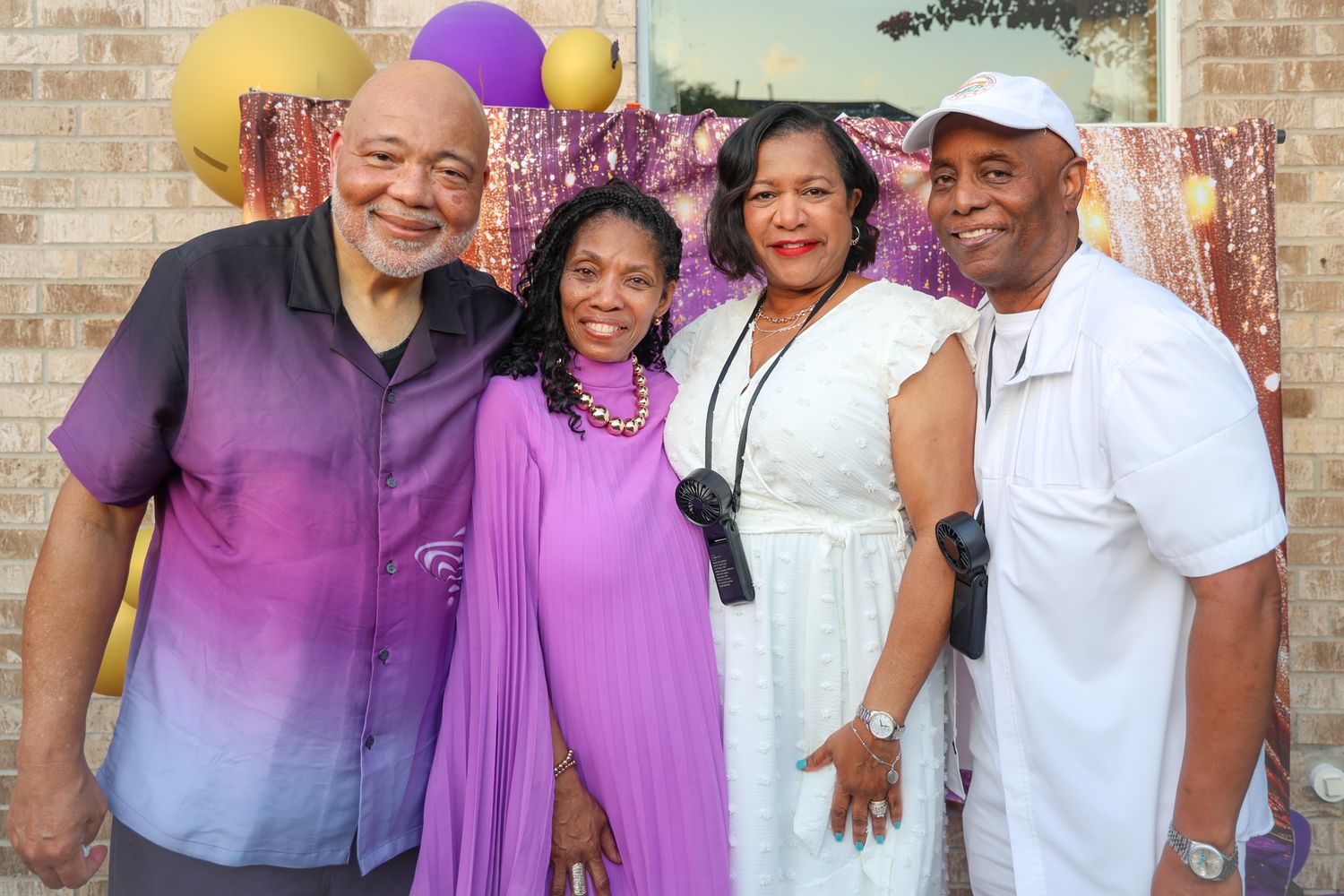 Four friends smiling together at a purple-themed celebration party outdoors.