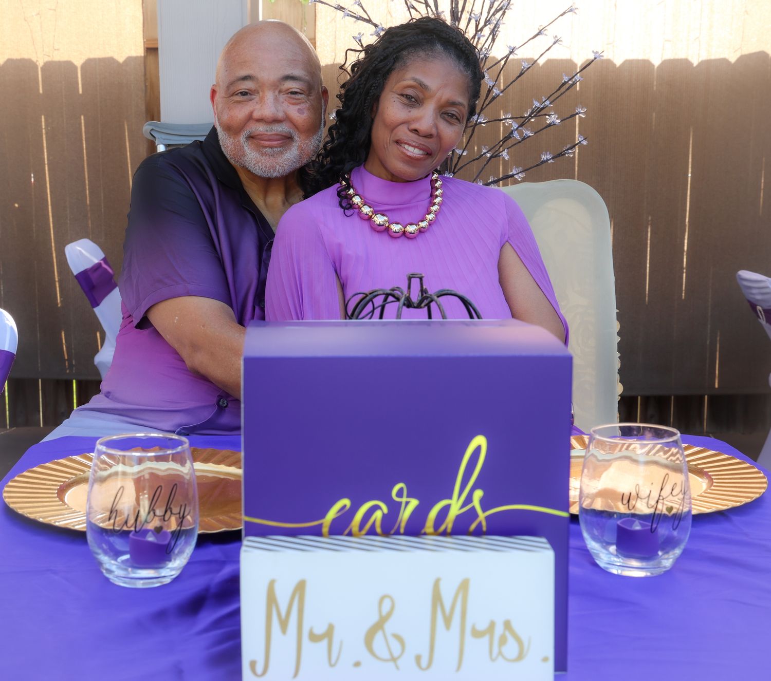 Couple in purple poses at Mr. & Mrs. cards table at wedding reception.