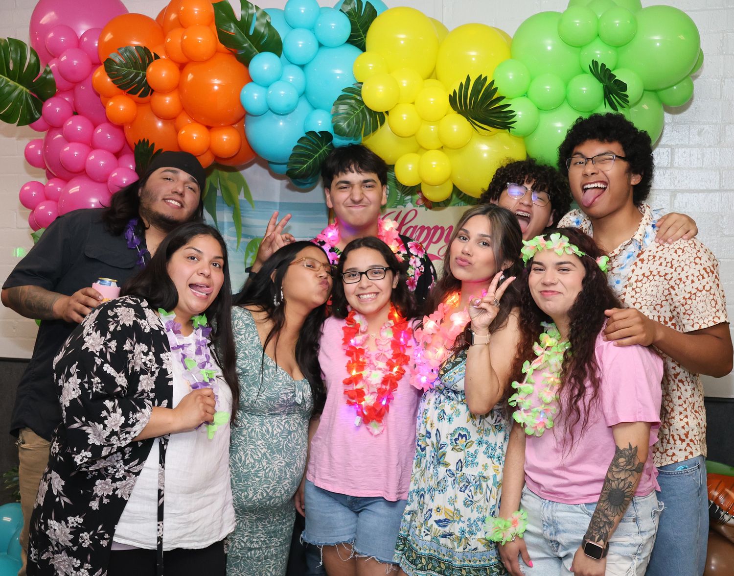 Guests pose with colorful balloon decorations at a tropical-themed party.