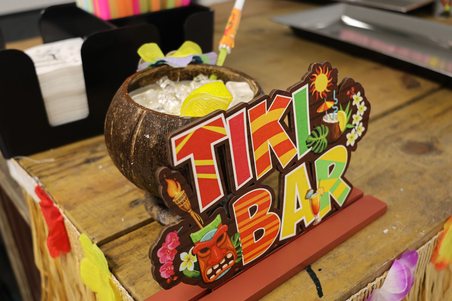 Wooden tiki-themed party sign with colorful tropical decorations.