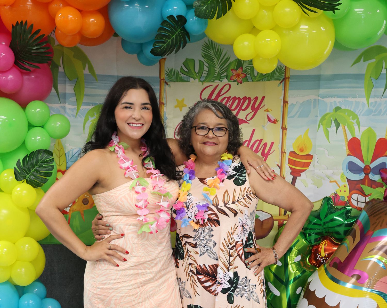 Tropical party setup with rainbow balloon arch and palm leaf decorations.