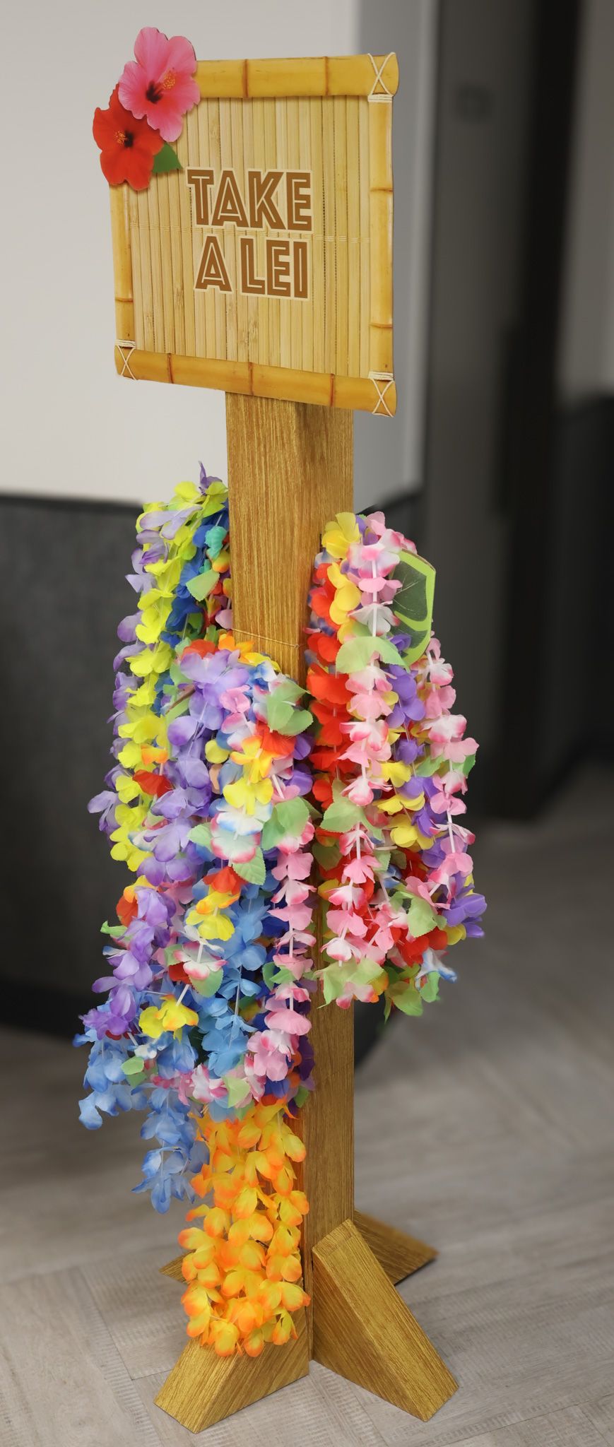 Wooden display stand decorated with colorful lei flowers and tropical signage.