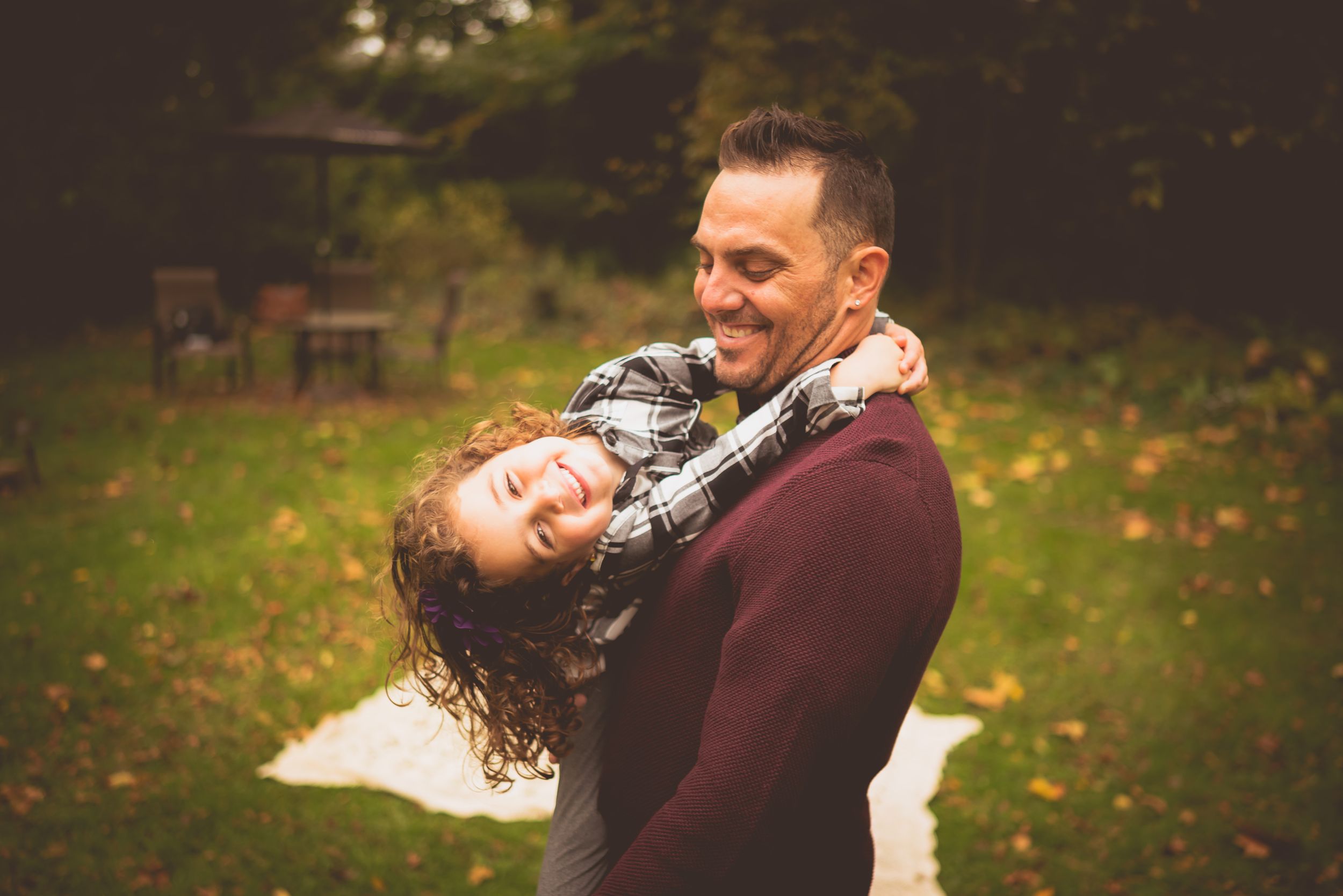 Playful parent swinging child upside down while laughing together in autumn garden.