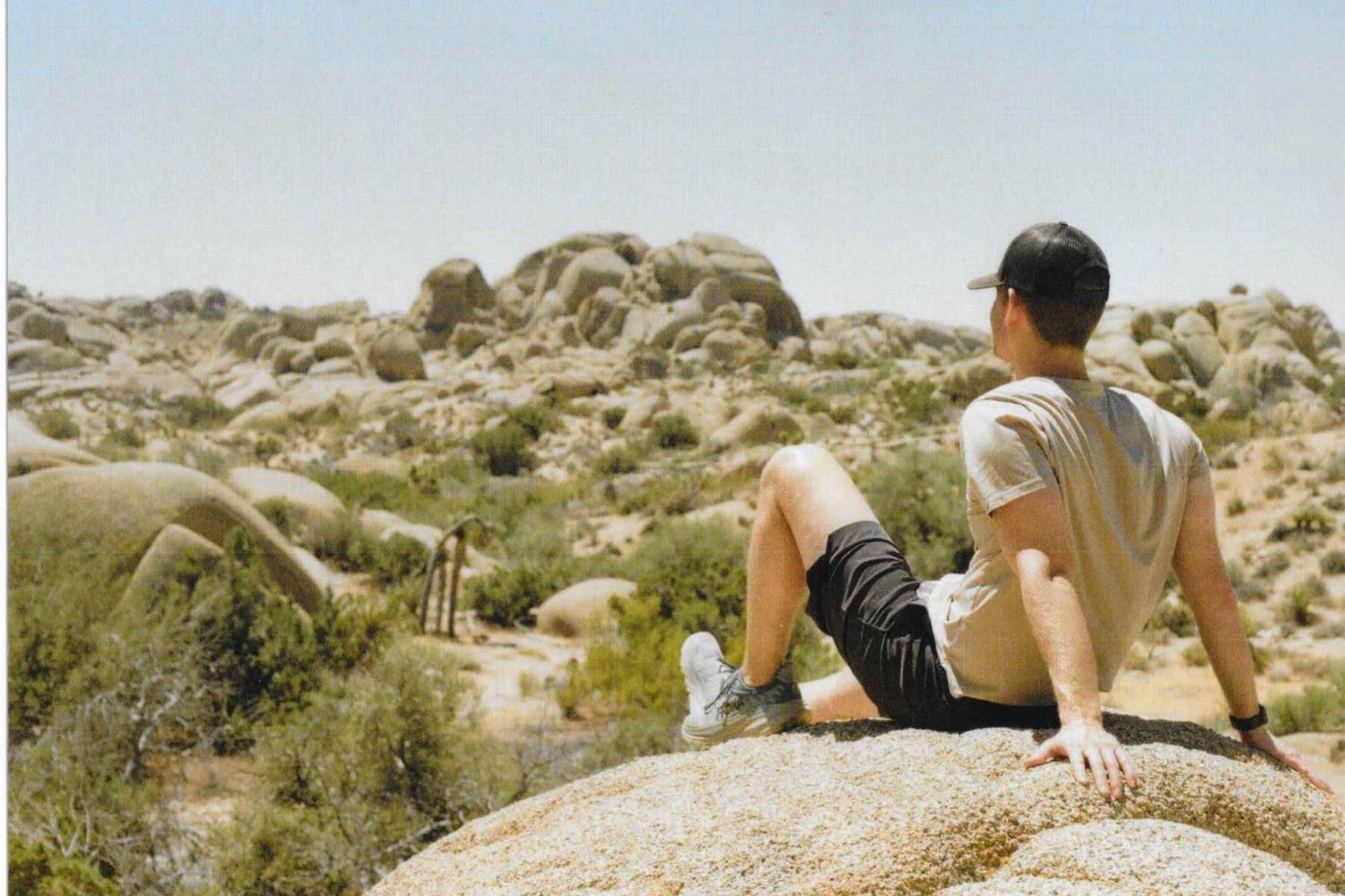 A hiker sitting on a rock during a hike in Joshua Tree National Park. Photographed on a 35mm film camera. Desert landscape with many cacti