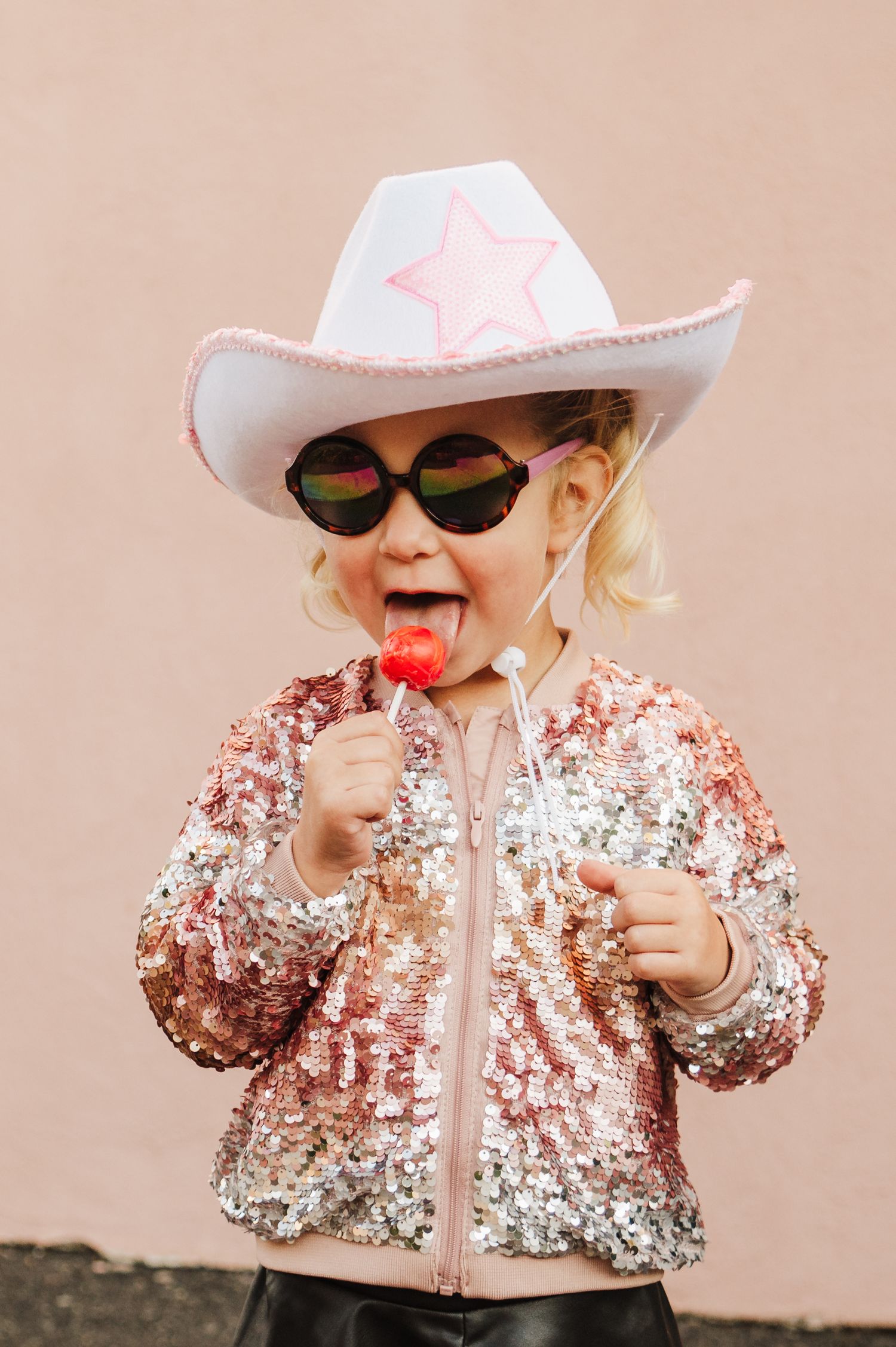Child wearing a sparkly pink jacket, white cowboy hat and sunglasses in a fun photo series.