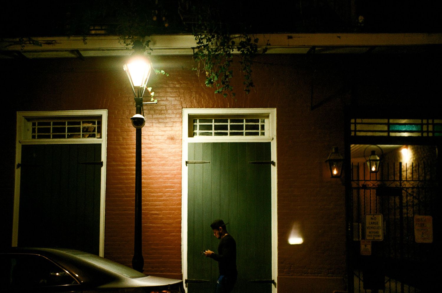 A dimly lit brick building facade at night with a street lamp casting shadows on green doors.