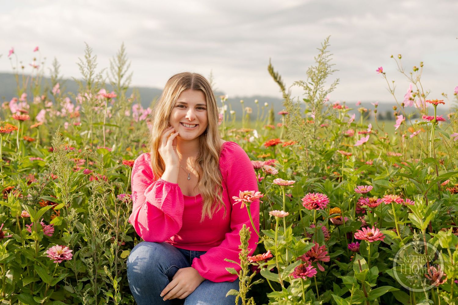 A portrait in a flower field with pink zinnias and mountains in the background.
