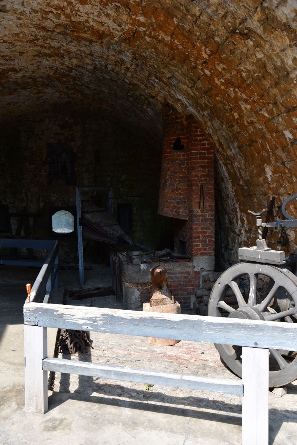 Inside view of an old brick fort tunnel with rustic wooden bench and wagon wheel under an arched stone ceiling.