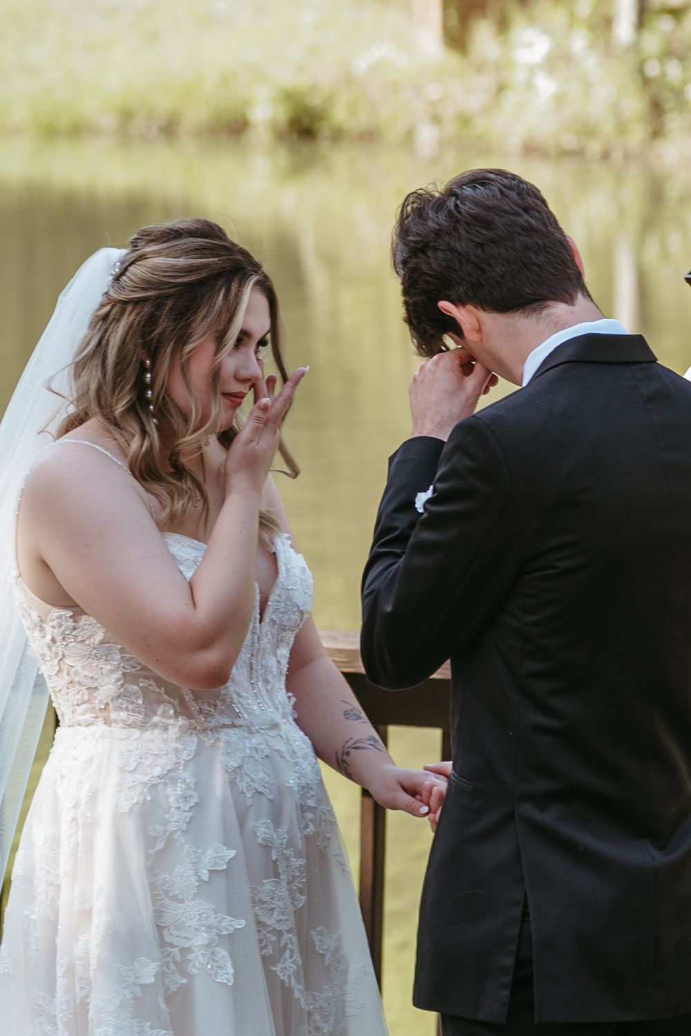 Emotional moment between couple during outdoor wedding ceremony by a lake.