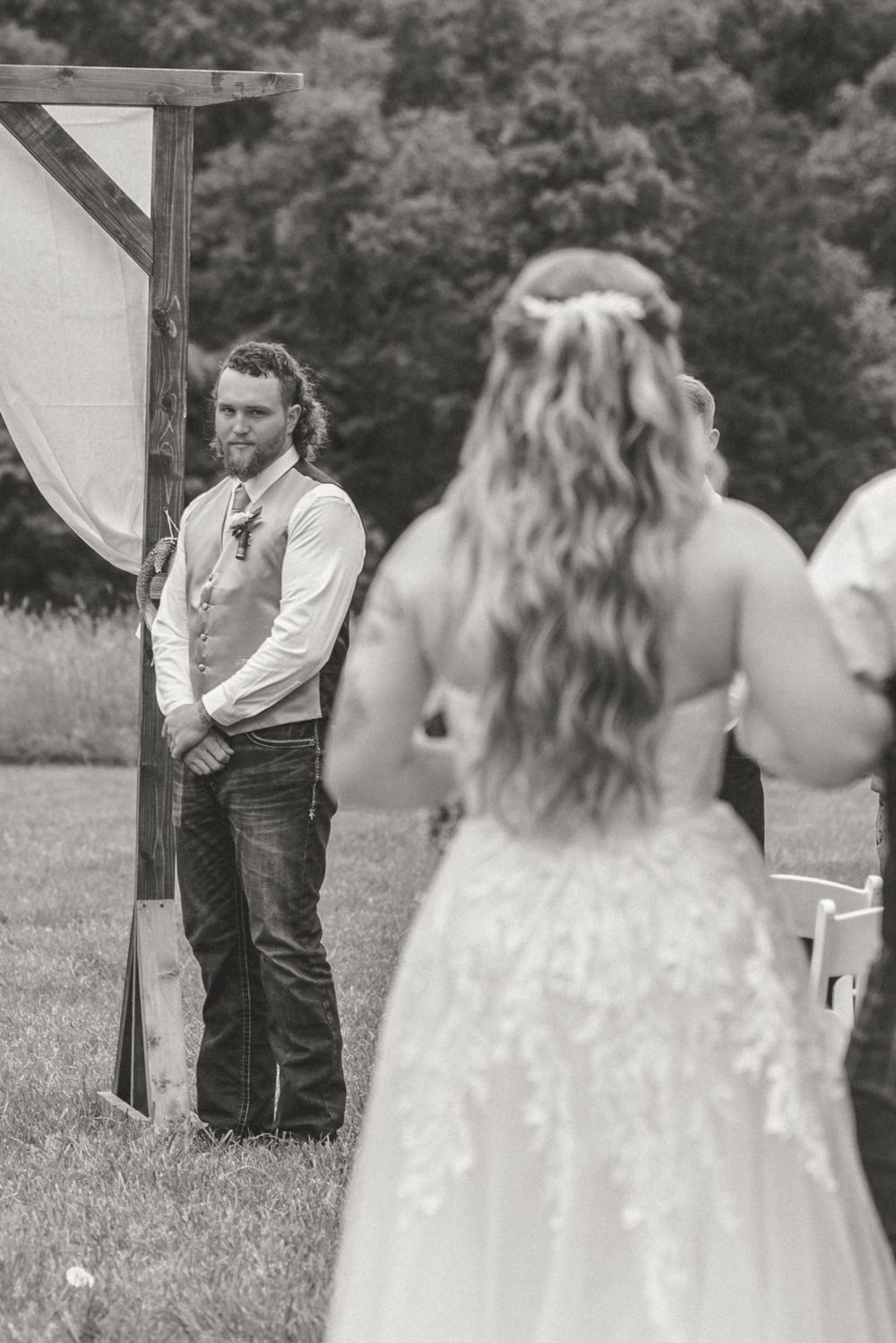 Black and white ceremony photo showing rustic outdoor wedding setting.