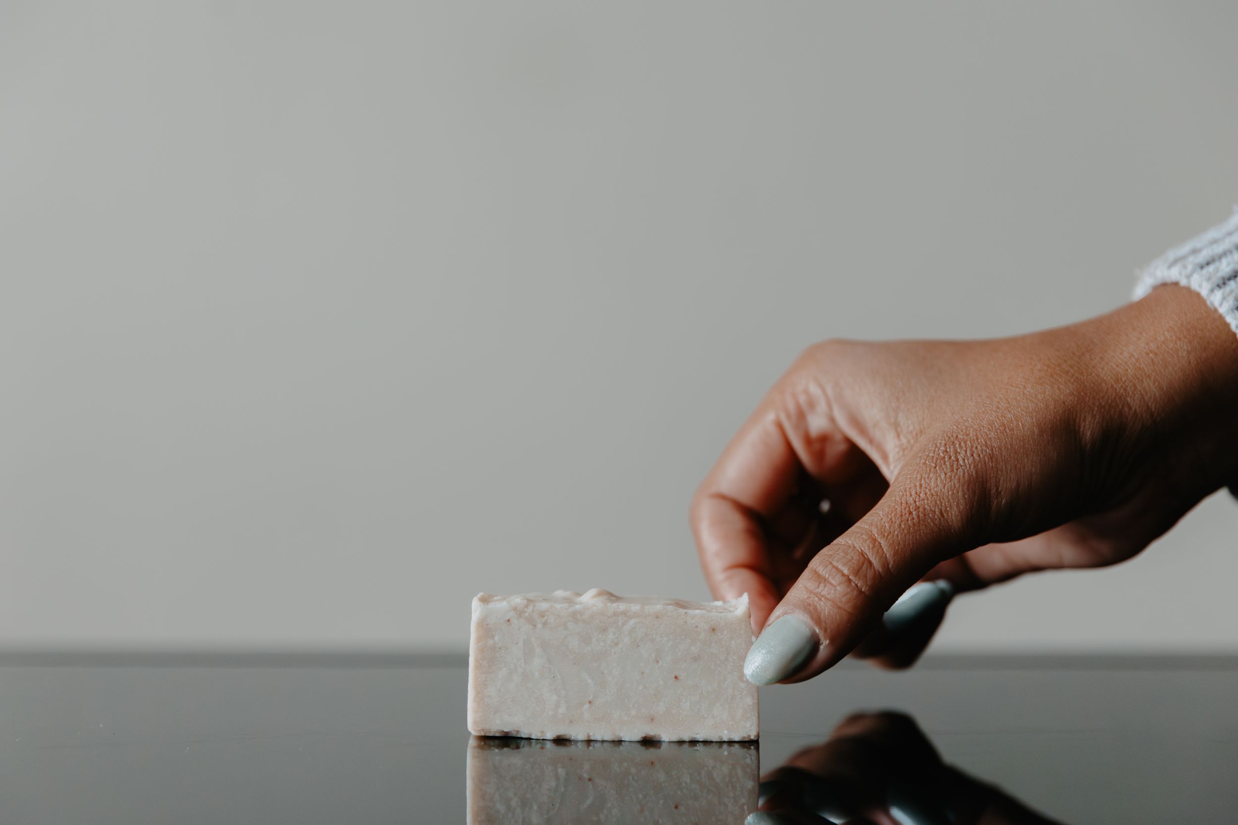 Hand holding a bar of handmade natural soap against a minimalist gray background.