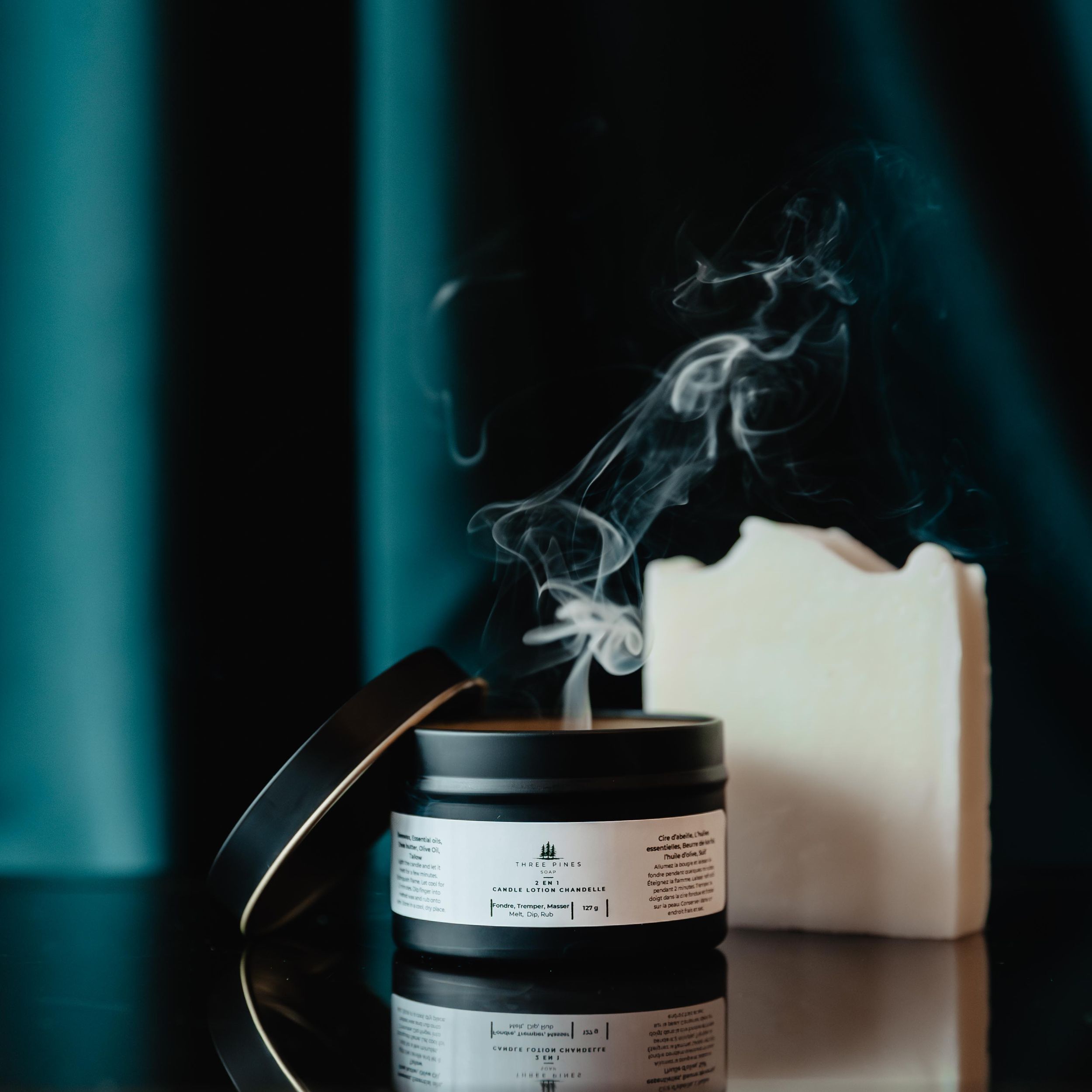 Artisanal candle with smoke rising against a dark teal background.