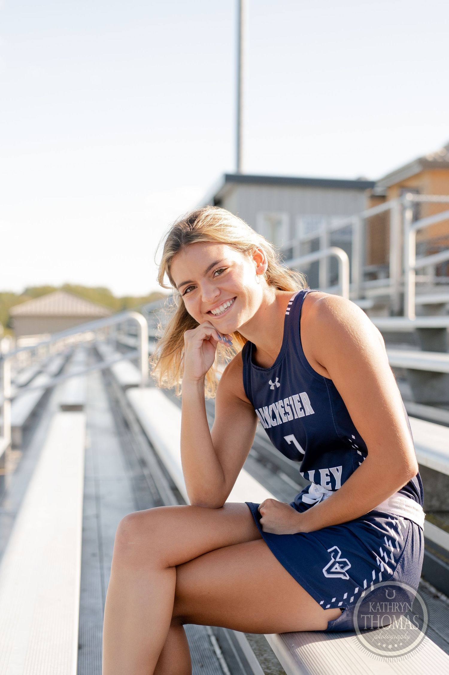 Field hockey player in navy uniform poses on stadium bleachers.