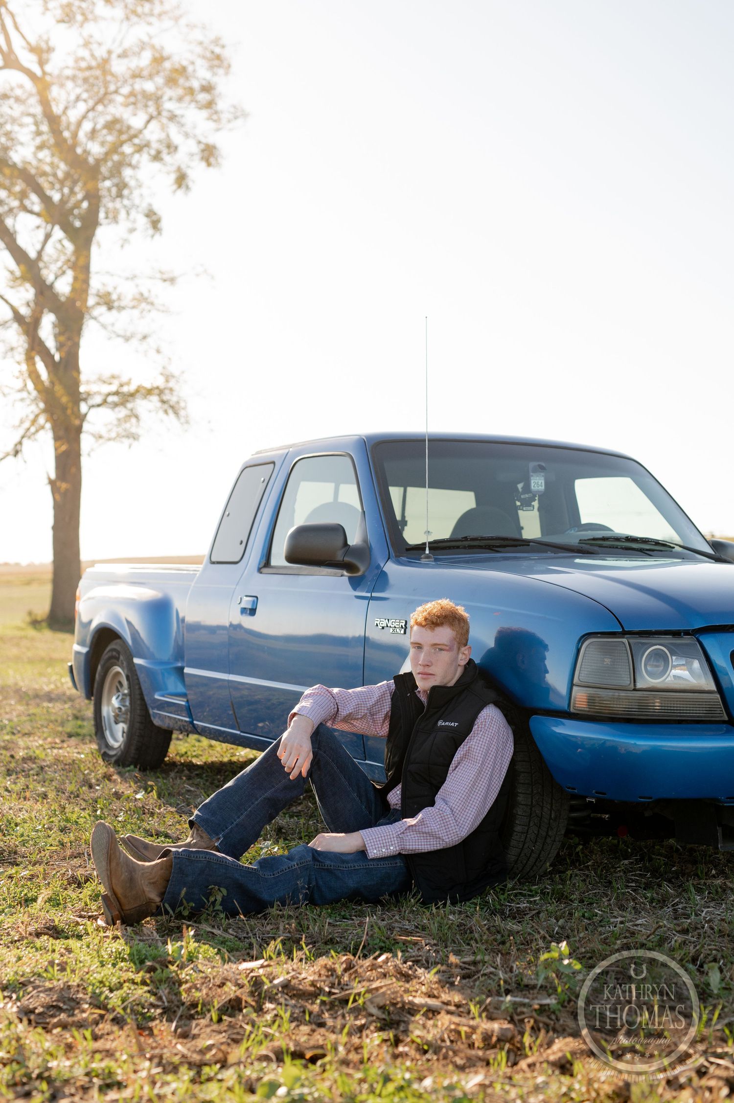 Someone sitting beside a blue Ford Ranger pickup truck in an autumn field.
