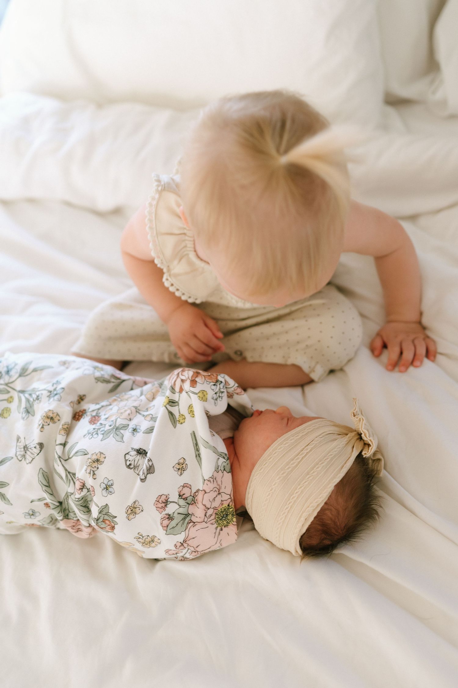 Two children resting together on white bedding with floral blanket.