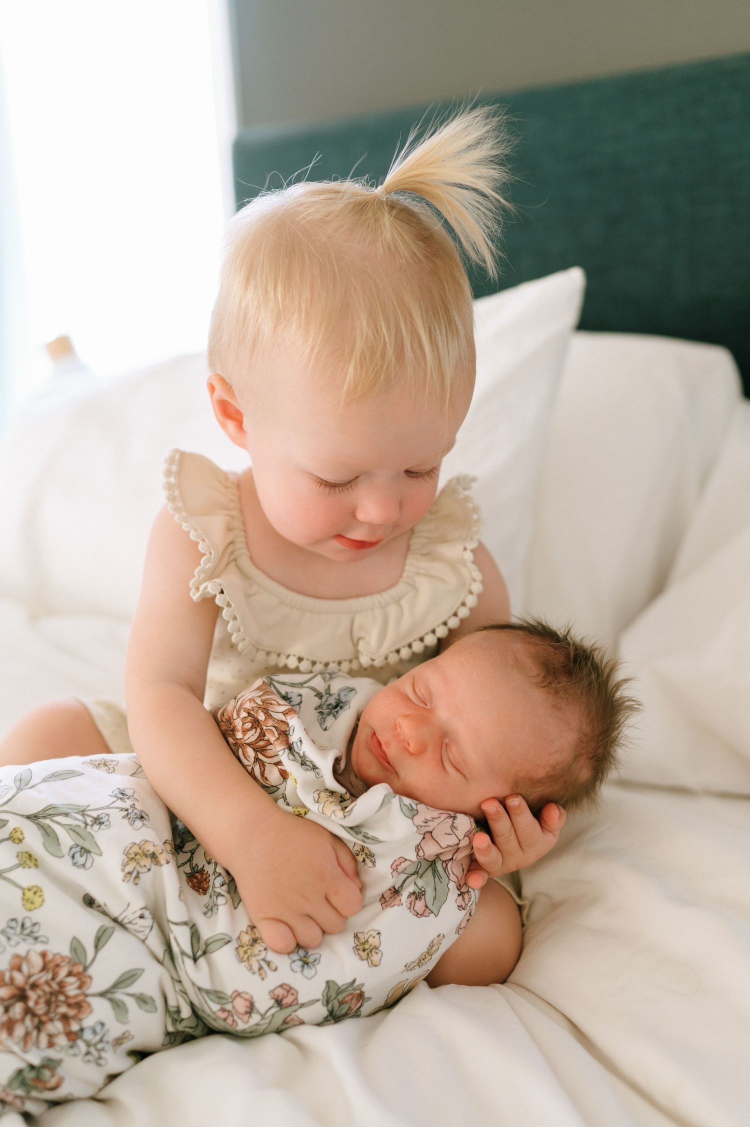Siblings share tender moment together on bed with white linens.