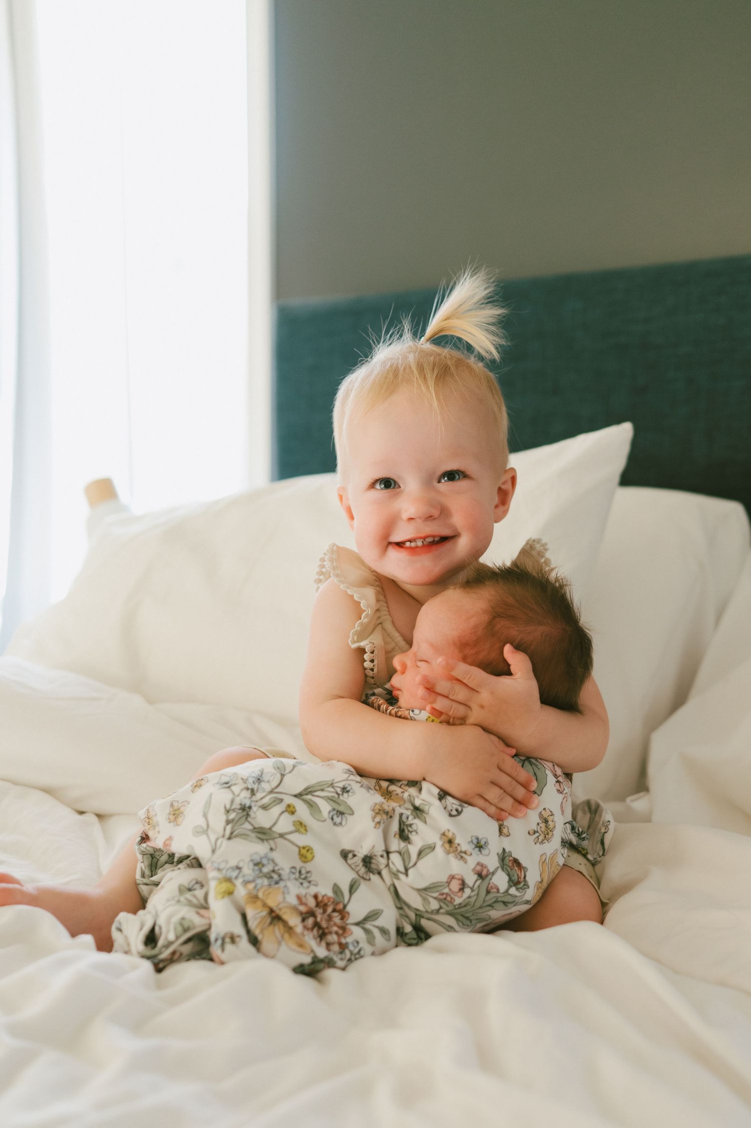 Joyful sibling moment captured on white bedding with green headboard.