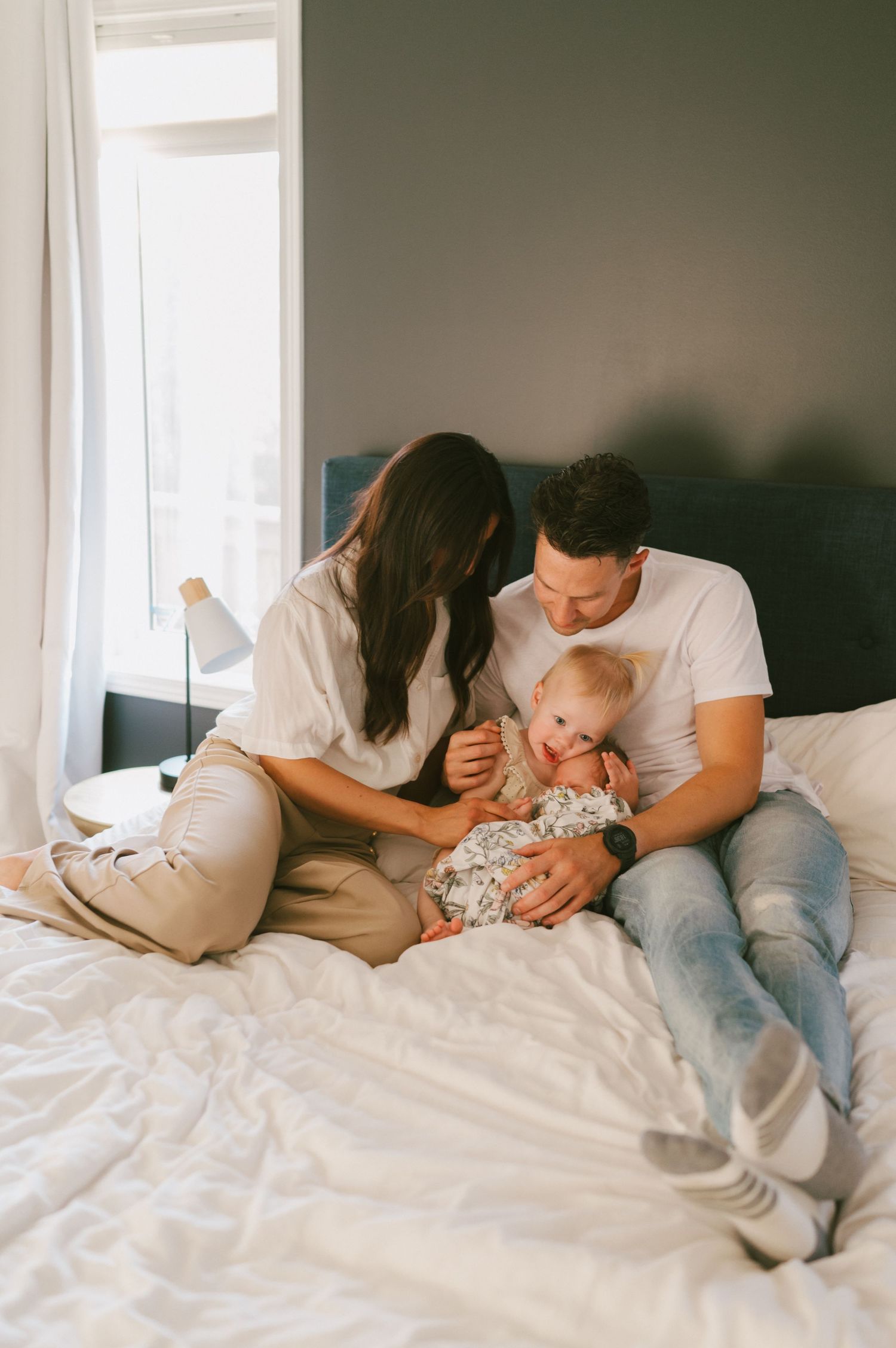 Family shares intimate moment together on bed near window.