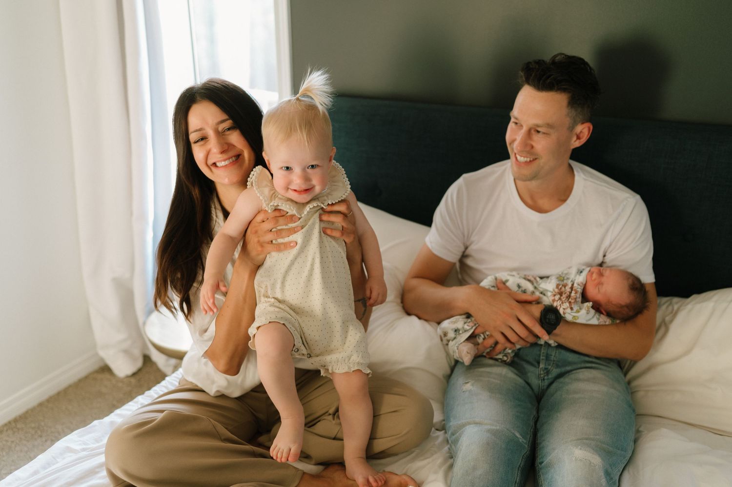A family relaxes together on a bed, sharing tender moments with their children in a naturally lit room.