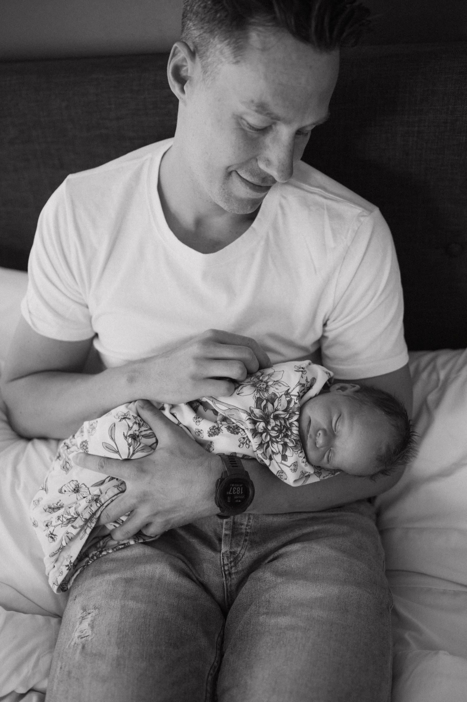 A touching black and white moment between a parent and newborn while resting on a bed.
