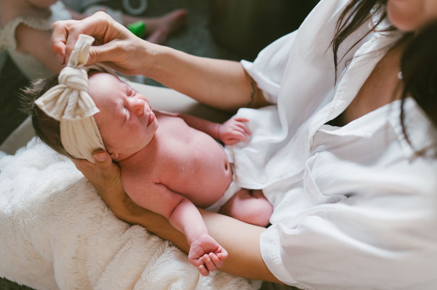 A gentle parenting moment with a newborn baby wearing a bow in soft natural light.