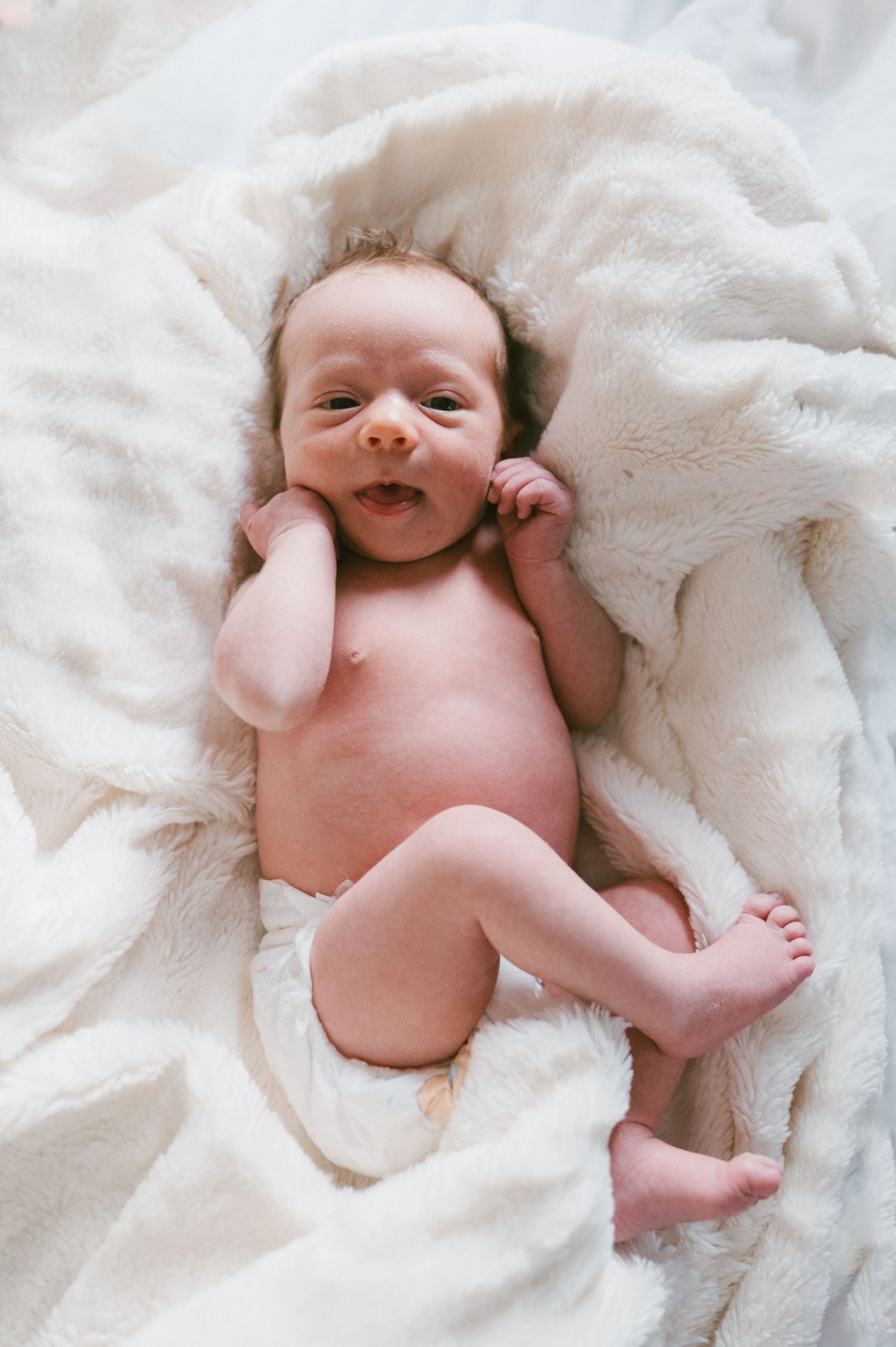 Happy smiling baby lying on soft white blanket.