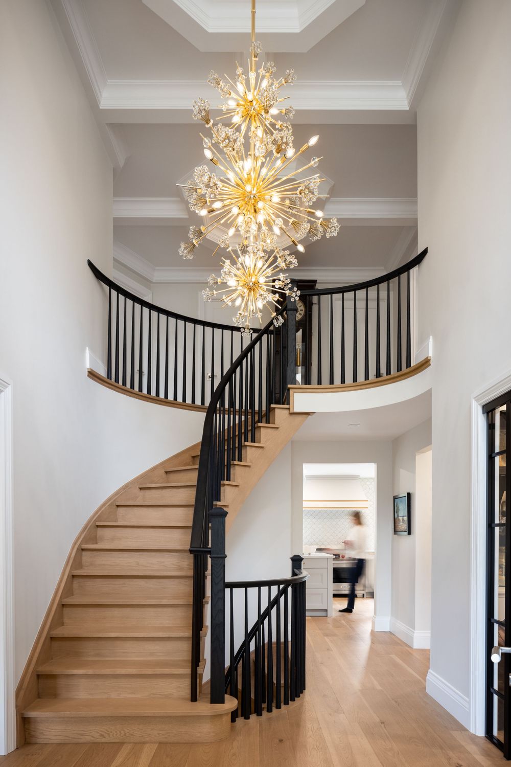 Modern curved staircase with wooden steps, black railings and dramatic sputnik chandeliers hanging in the entryway. Interiors Photography.