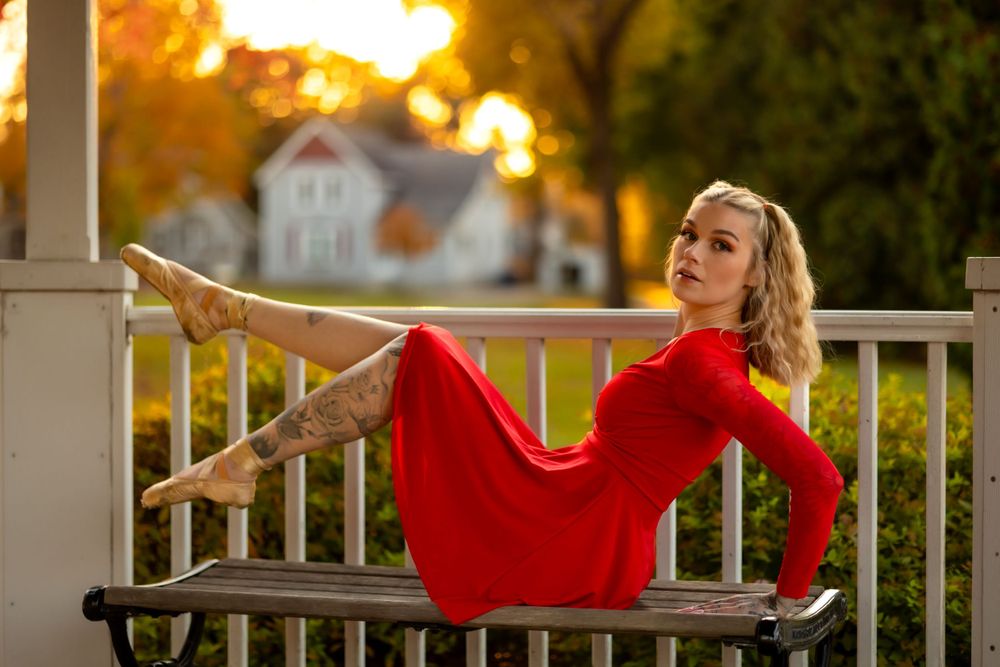 Person in red dress posing elegantly on porch railing at sunset.
