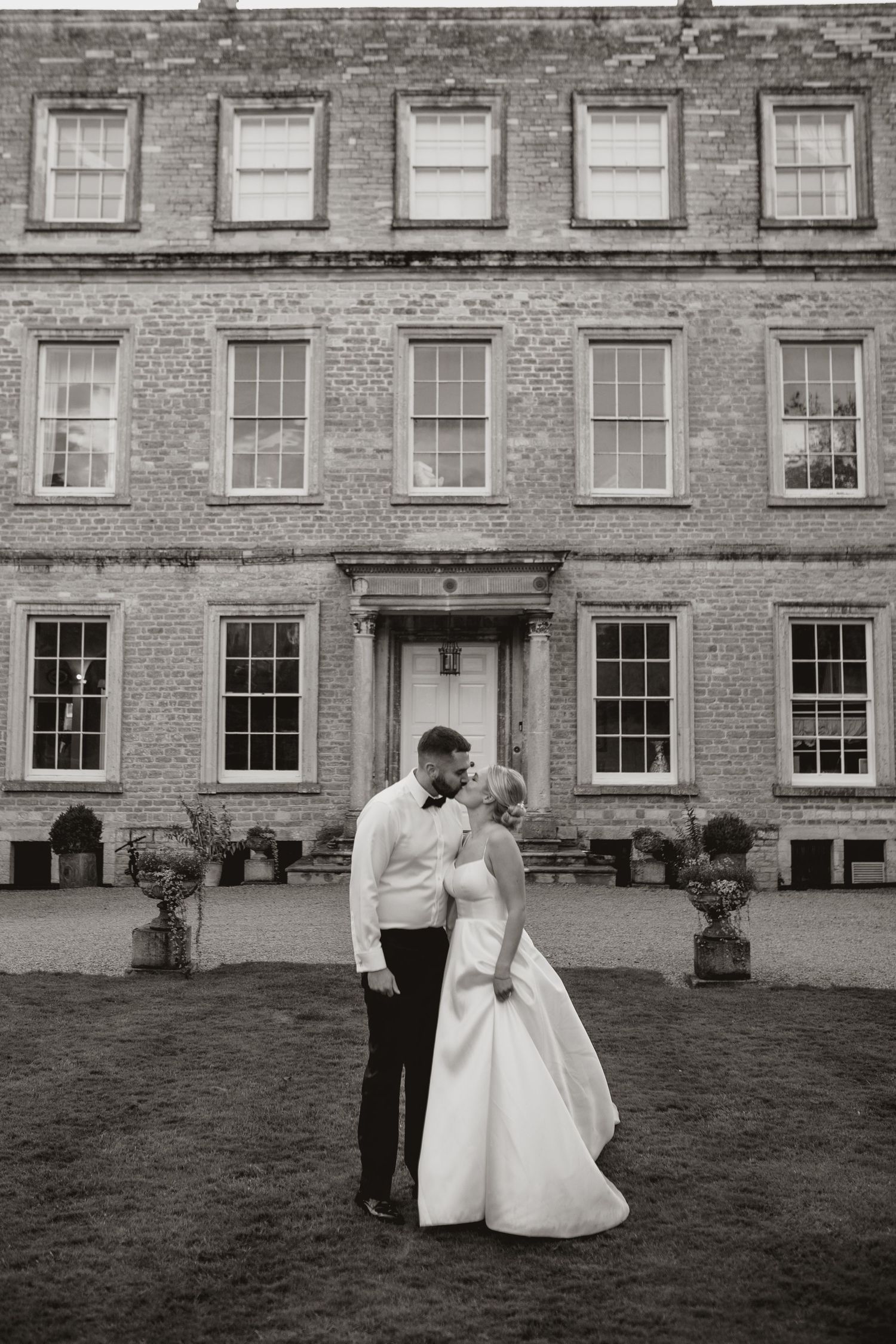 Newlywed couple sharing a moment in garden setting with brick wall and greenery backdrop.