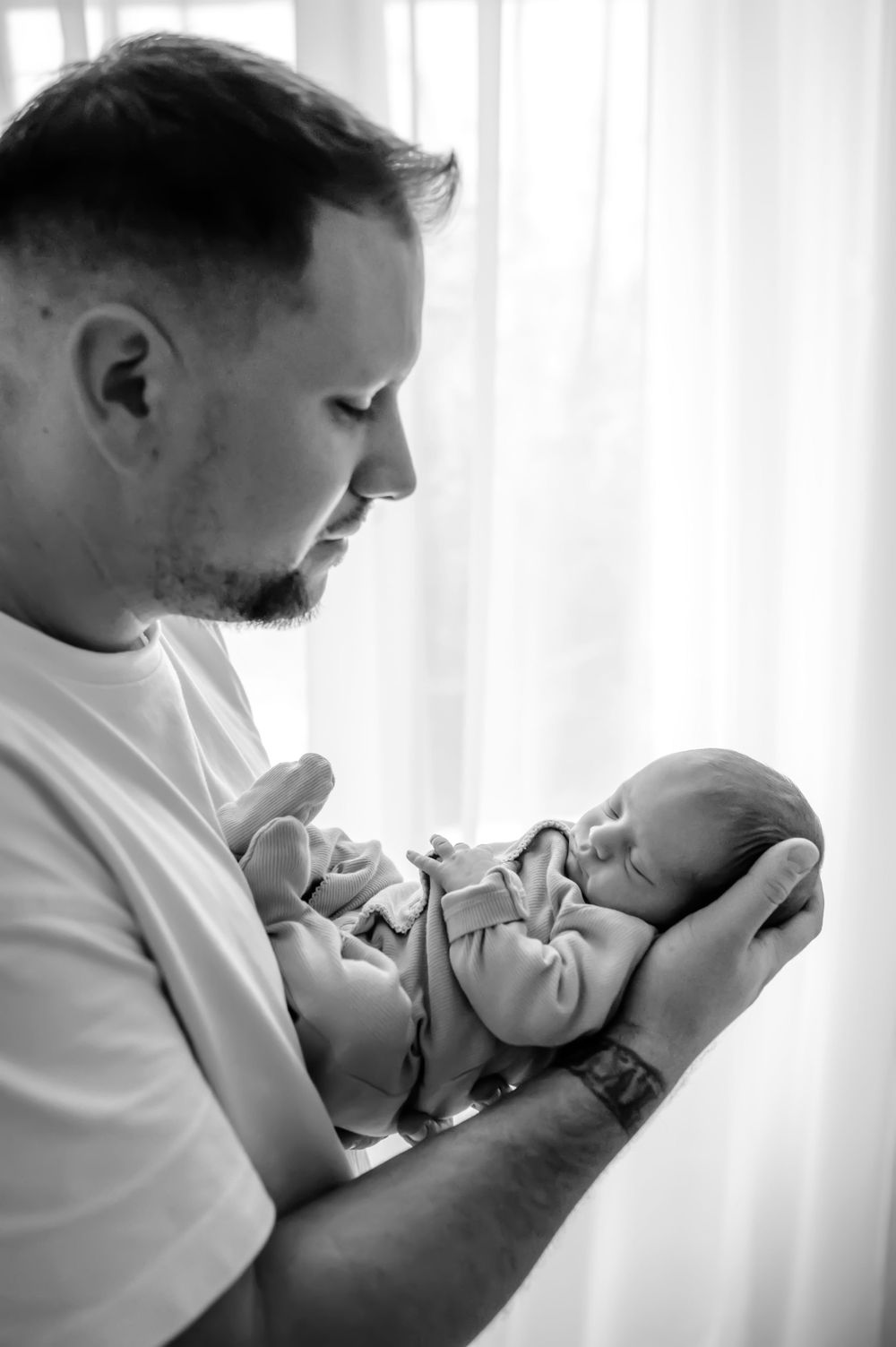 A touching black and white portrait of a father holding and gazing adoringly at his sleeping newborn baby.