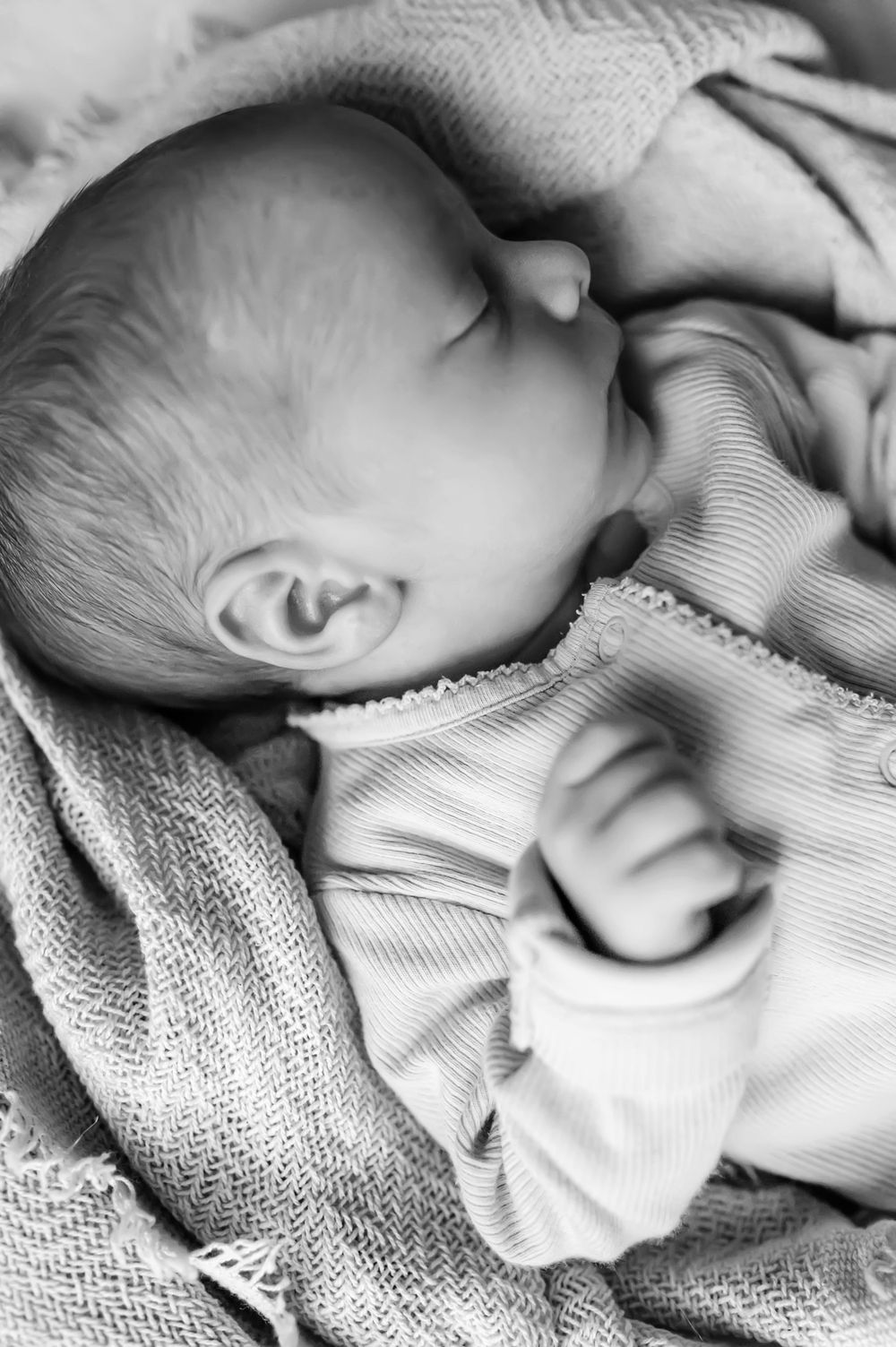 A sleeping baby swaddled in soft gray knit blankets and wearing light colored clothing rests peacefully.