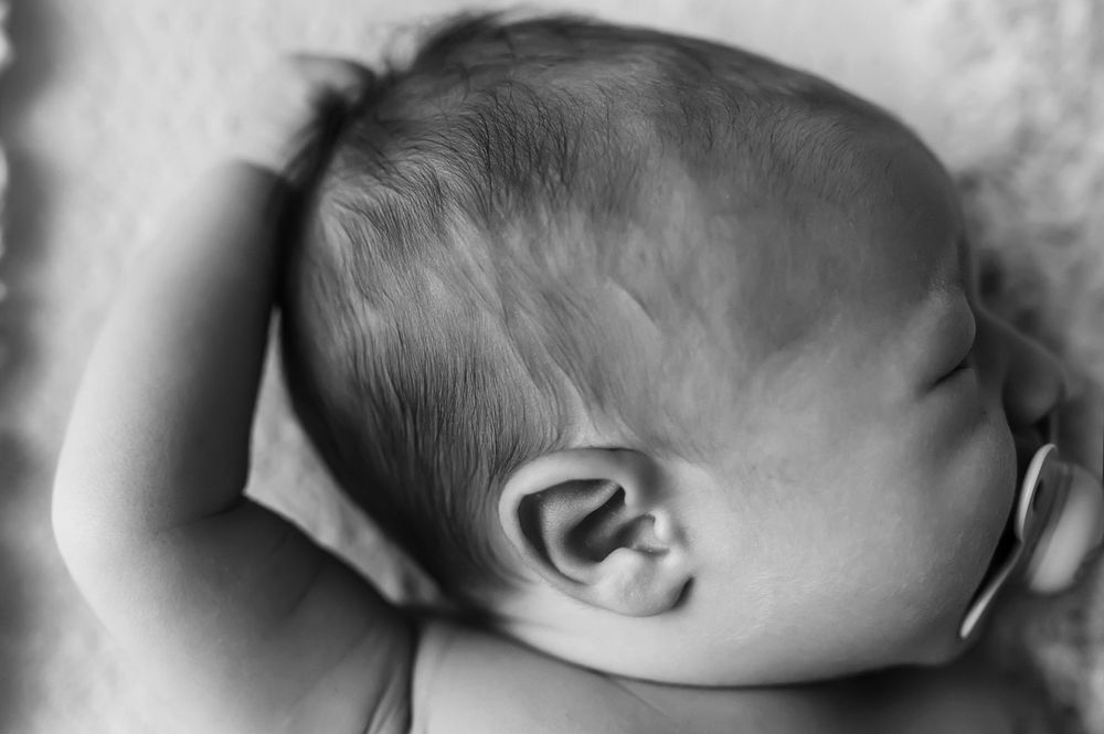 Close-up black and white profile view of a sleeping baby's head against a soft pillow.