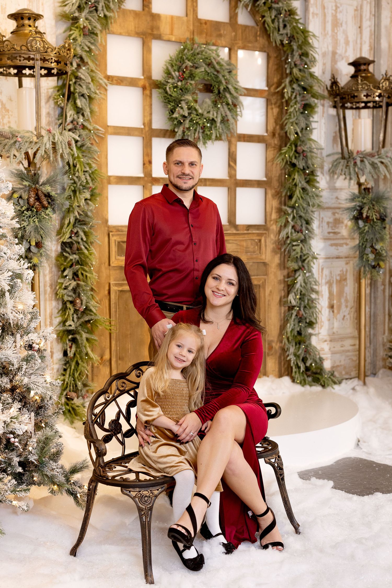 Christmas portrait with red and brown outfits in front of decorated door with wreaths, garland, and lanterns.