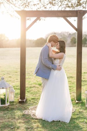 Romantic sunset wedding photos with couple embracing under wooden pergola.