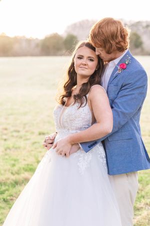 A romantic outdoor portrait session showing a couple embracing in a sun-lit field wearing a white dress and blue suit.