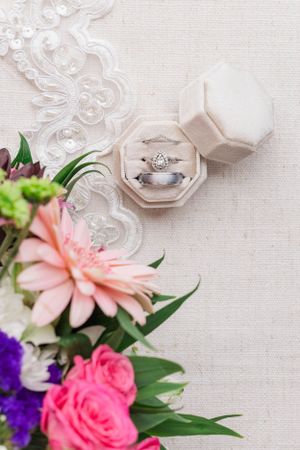 Wedding rings and delicate pink and purple flowers arranged on white linen with romantic lighting.