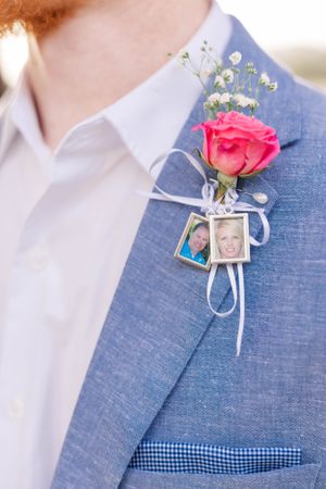 Pink rose boutonniere with small photo charms pinned to a blue suit jacket.