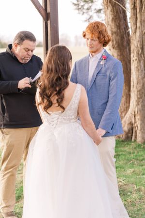 Wedding ceremony in progress with guests gathered under rustic wooden arbor.