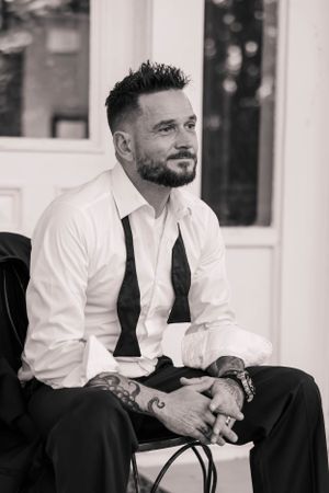Black and white portrait of a groom in formal attire sitting casually.