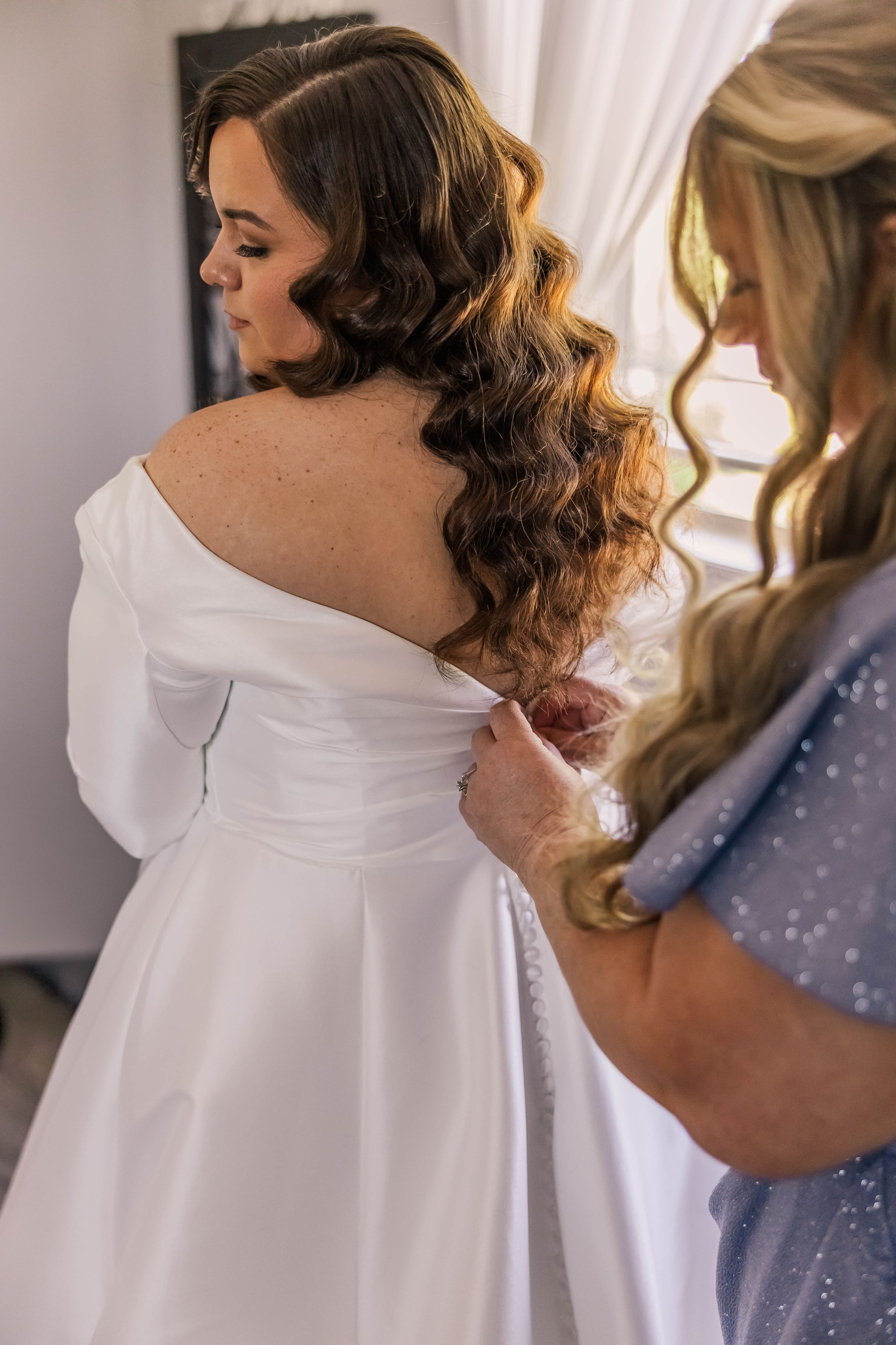 Wedding dress being adjusted in soft natural light during bridal preparations.