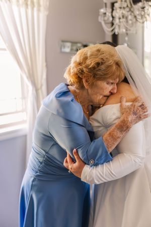 Emotional first look moment between bride in white dress and family member in light blue dress.