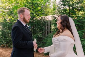Outdoor wedding ceremony under green trees with couple exchanging vows.